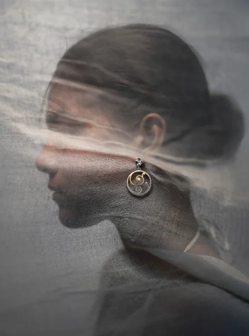 Portrait behind sheer fabric wearing filigree earrings with gold accent
